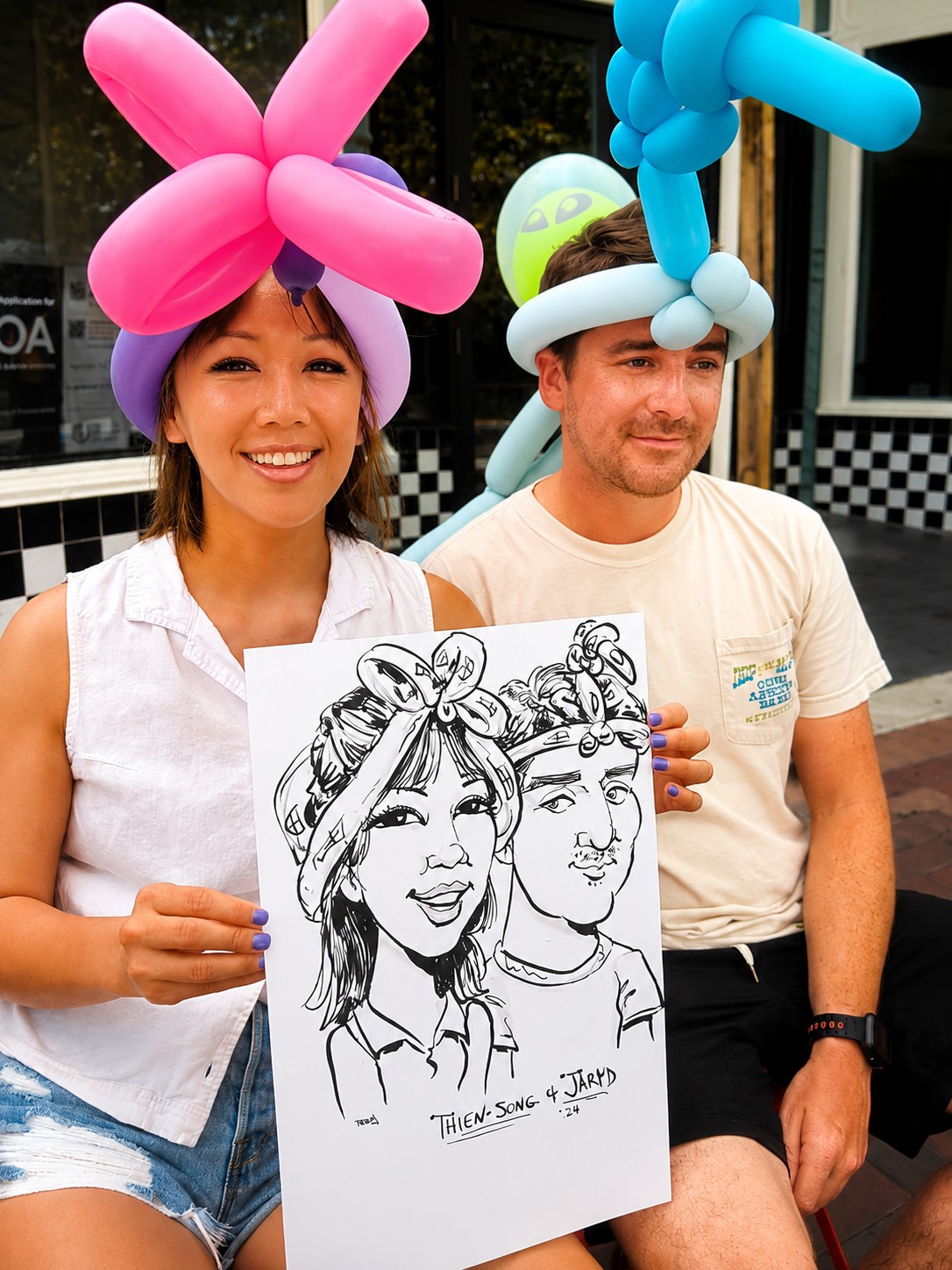 Couple wearing balloon hats holding a duo caricature at a downtown Houston community event