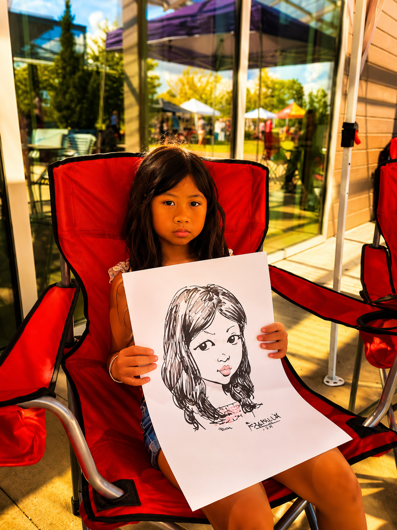 Young girl holding her black-and-white caricature at an outdoor summer community festival